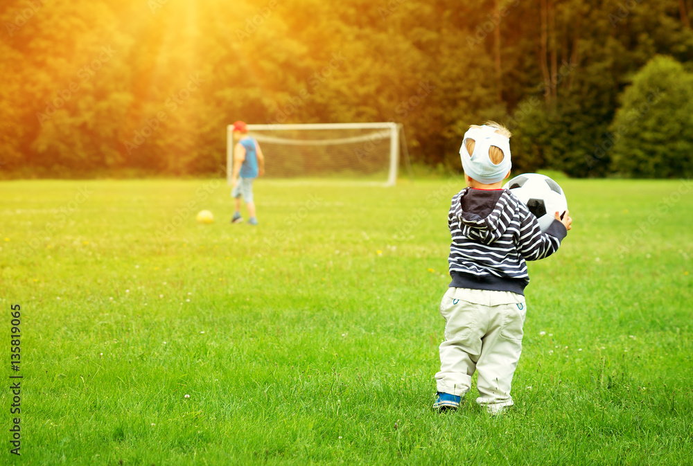 Little boy playing football on the field with gates