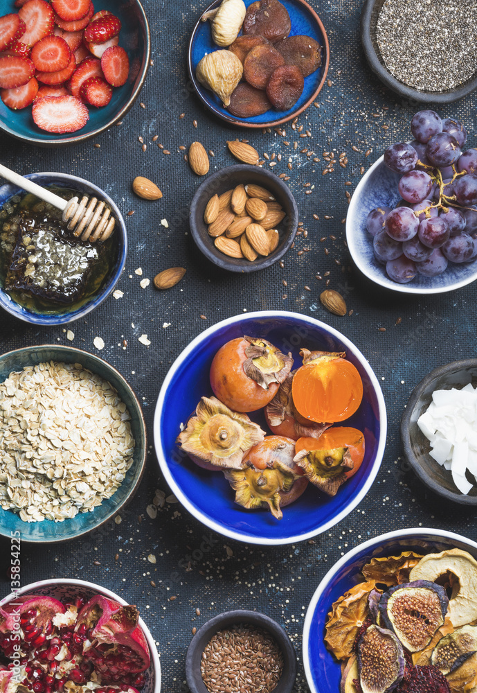 Ingredients in bowls for healthy breakfast over dark blue background, top view. Fresh and dried frui