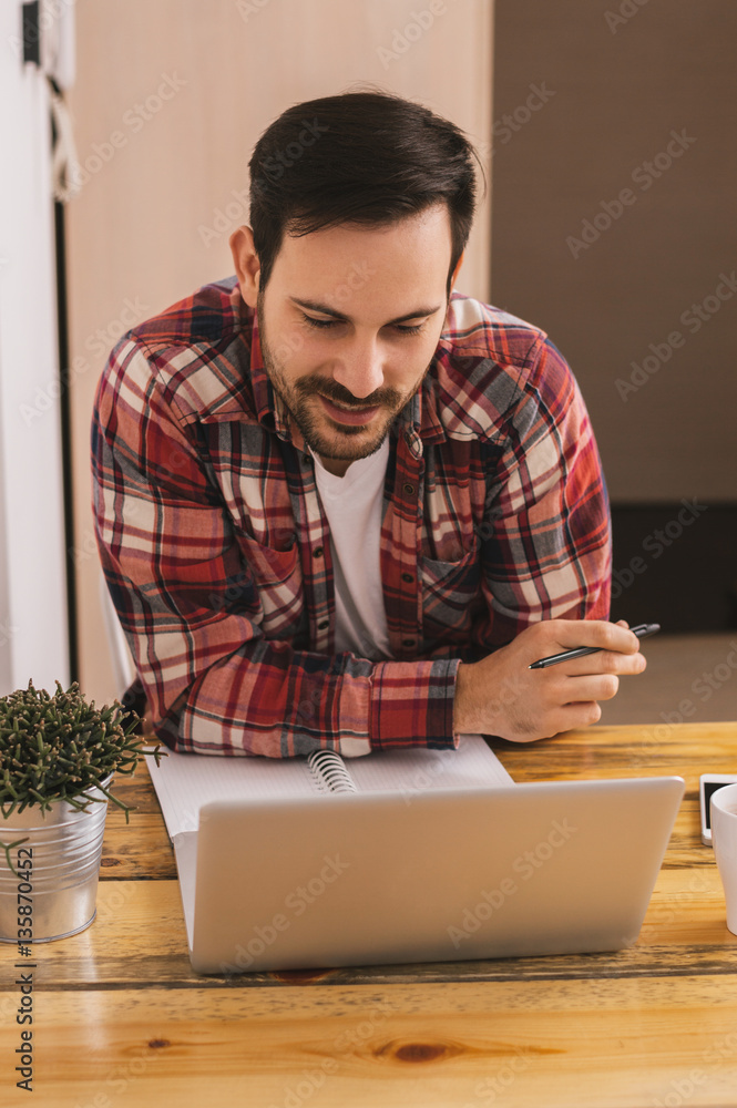 Handsome man working on laptop at home office.