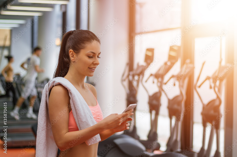 Active girl using smartphone in fitness gym