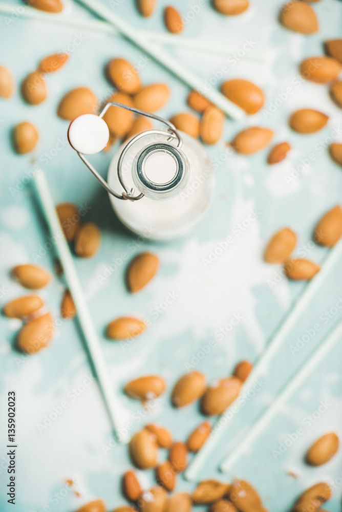 Dairy alternative milk. Almond milk in bottle and fresh nuts over blue background, top view, selecti