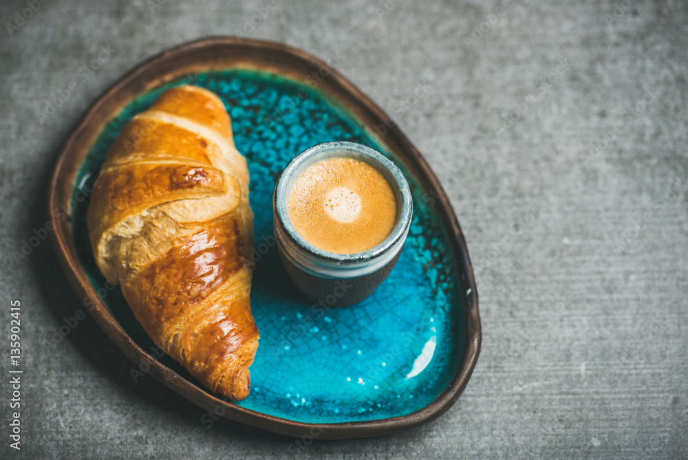 Cup of espresso coffee and croissant in turquoise blue ceramic tray over grey concrete background, s