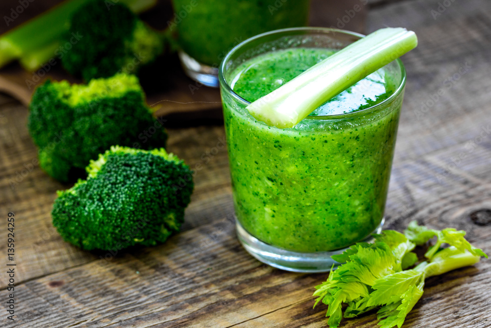 Green vegetable smoothie in glass at wooden background