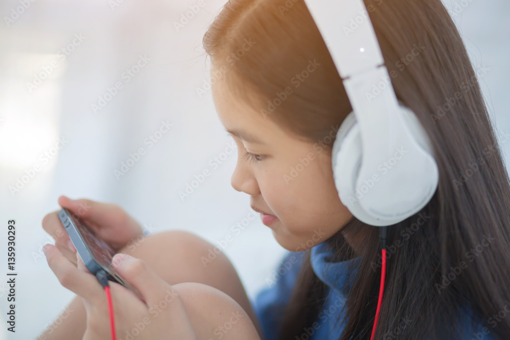 Pretty Asian girl using headphone for listen music by smartphone on the bed in her bedroom