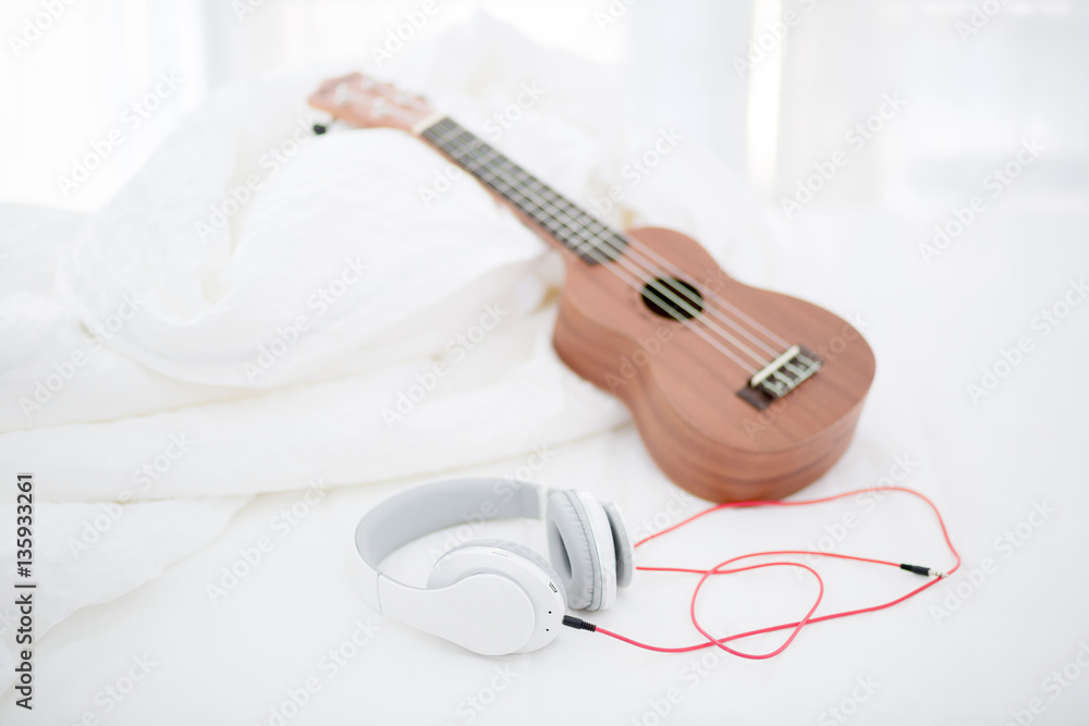 Classic Ukulele guitar on bed with headphone