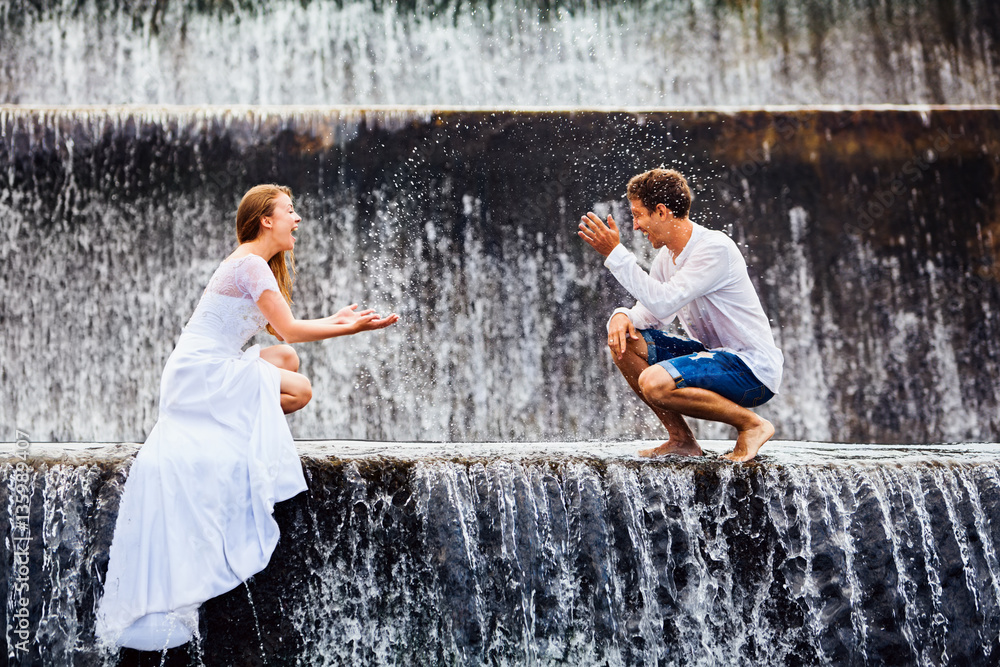 Happy family on honeymoon holidays - married loving couple splashing with fun under falling water in