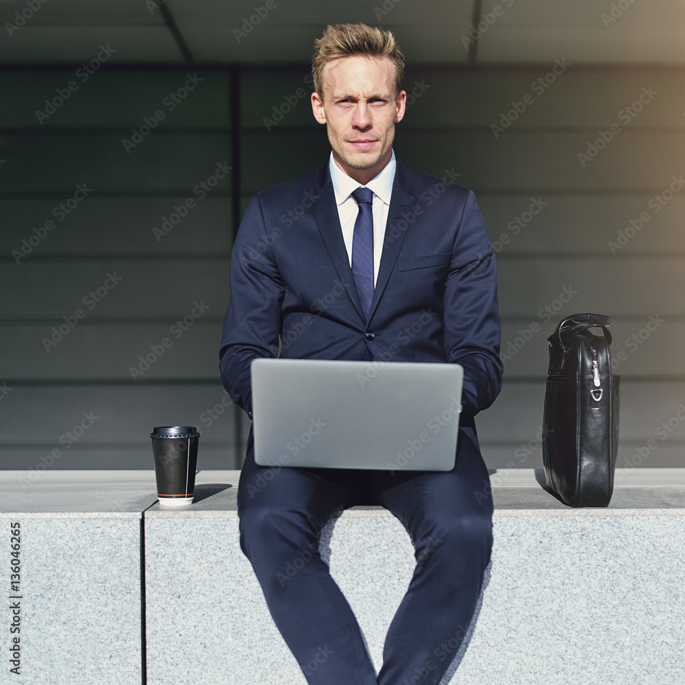 Handsome businessman with laptop looking at camera