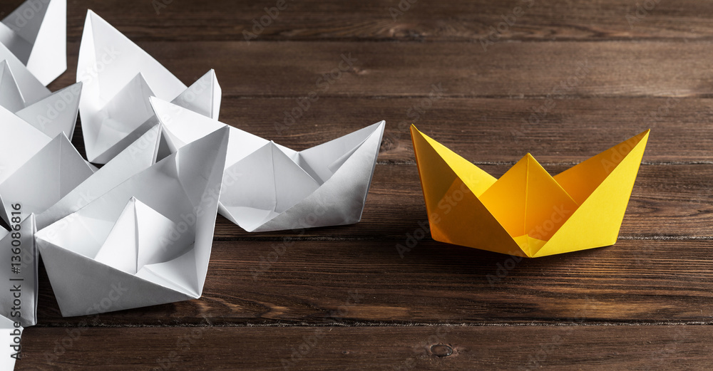 Business leadership concept with white and color paper boats on wooden table