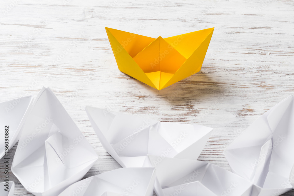 Business leadership concept with white and color paper boats on wooden table