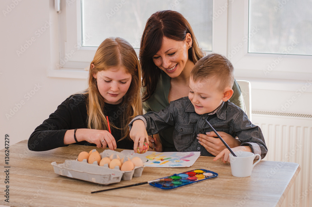 Young mother and her two kids painting Easter eggs