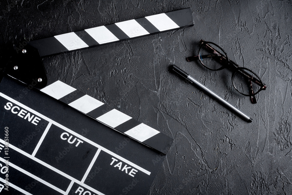 Screenwriter desktop with movie clapper board dark background top view