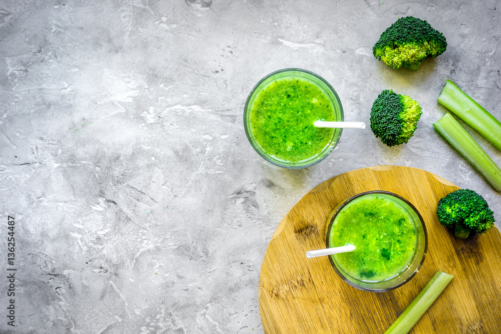 Green vegetable smoothie in glass at gray background top view