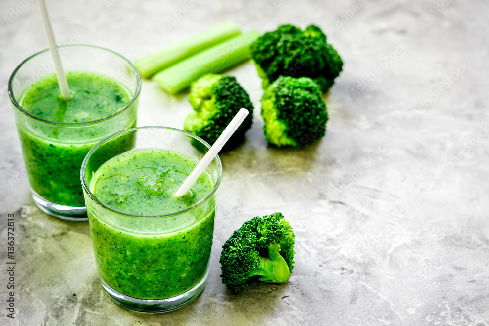 Green vegetable smoothie in glass at gray background