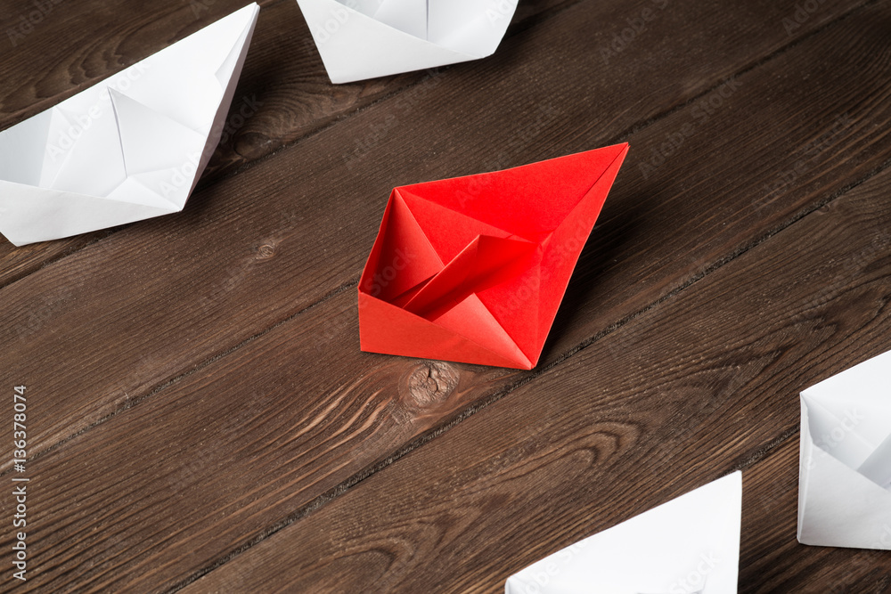 Business leadership concept with white and color paper boats on wooden table