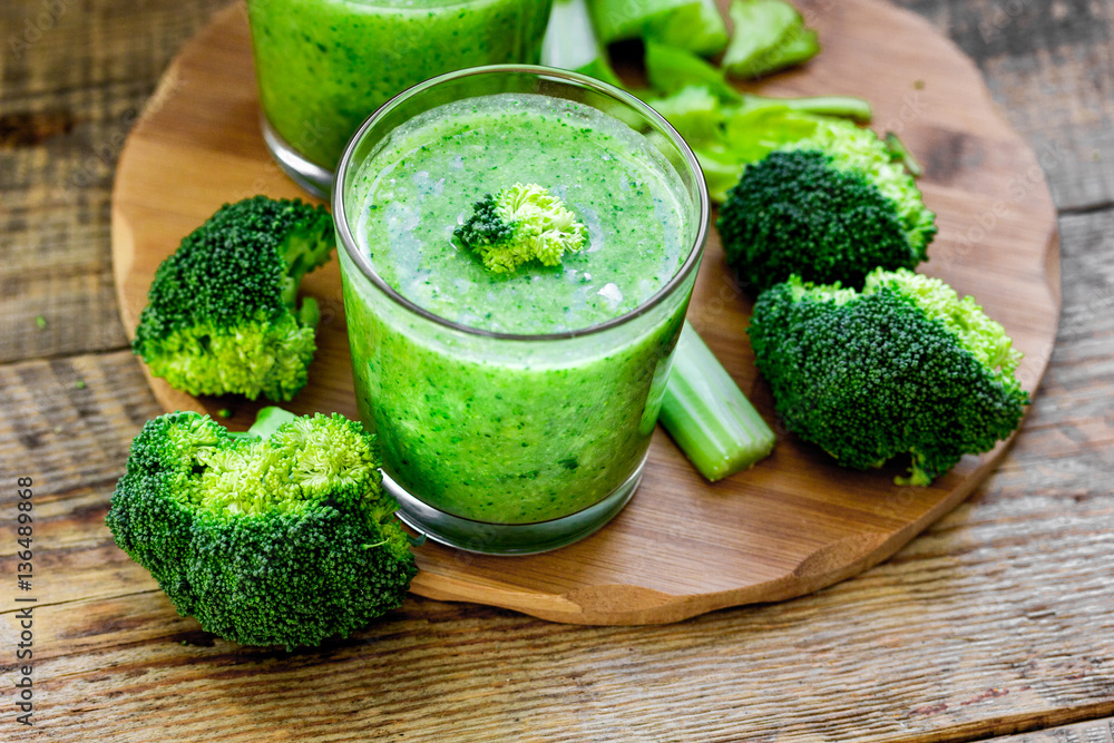 Green vegetable smoothie in glass at wooden background