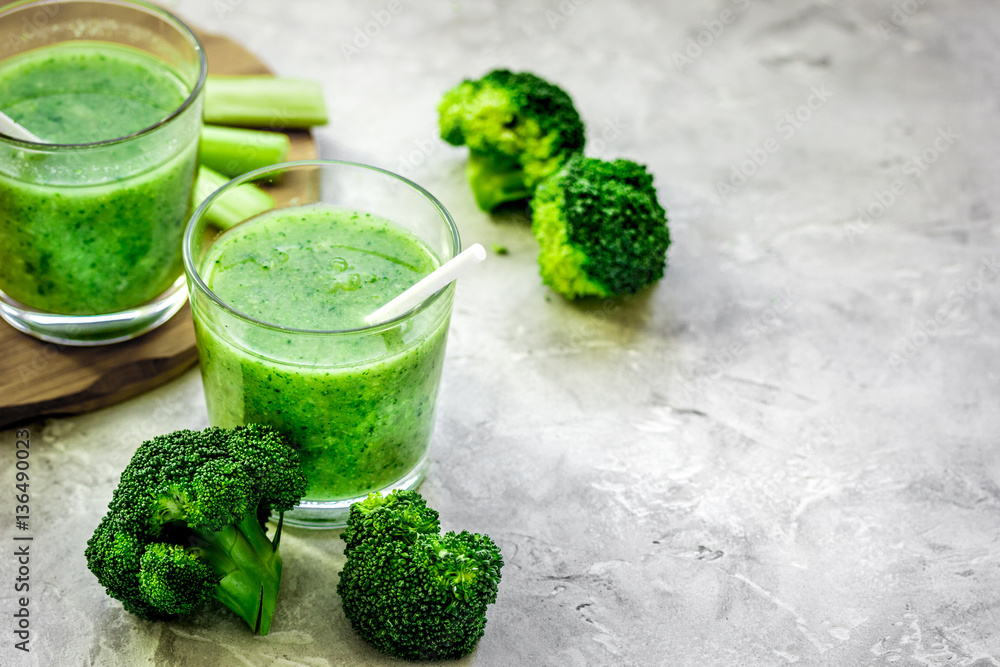 Green vegetable smoothie in glass at gray background