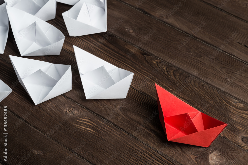 Business leadership concept with white and color paper boats on wooden table