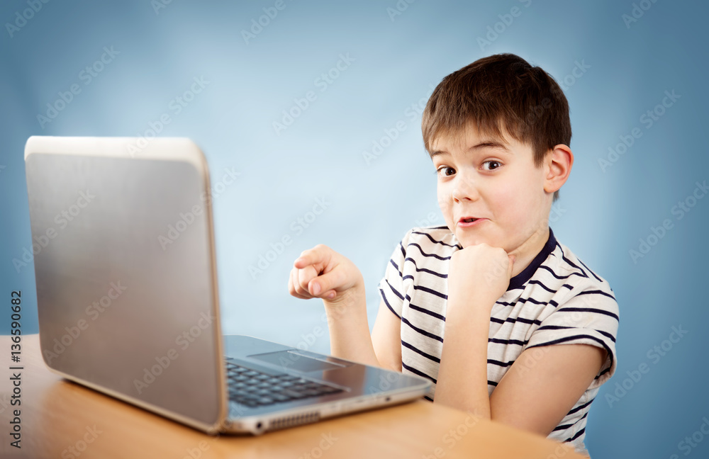 surprised seven years old child sitting with a laptop at table