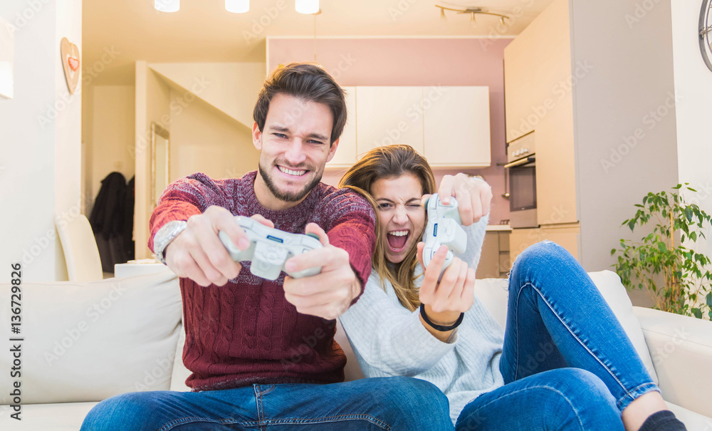 Happy couple playing videogame at home on the sofa.