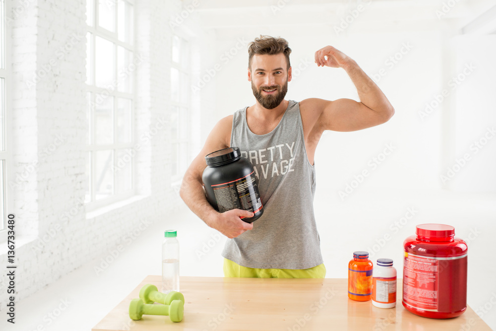 Portrait of athletic man in sportswear with proteins and vitamins in the white gym interior