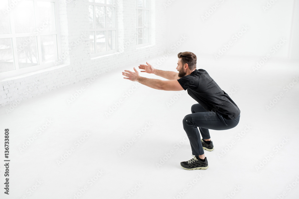 Handsome man in the black sportswear holding plank in the white gym interior