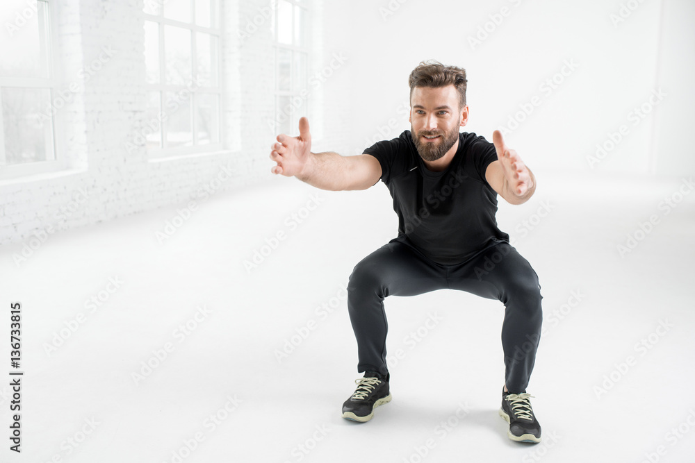 Handsome man in the black sportswear holding plank in the white gym interior