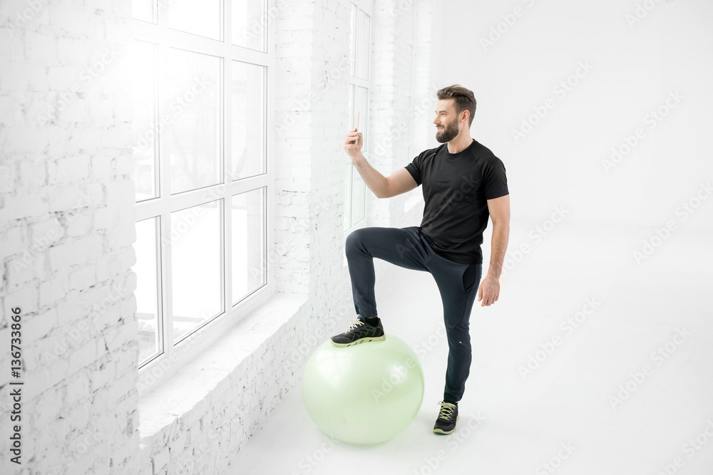 Handsome man in the black sportswear making selfie portrait with phone standing in the white gym int