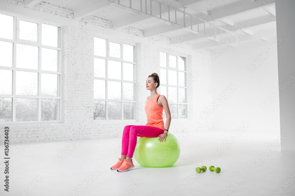 Young woman in colorful sportswear doing fitness with fitness ball in the white gym