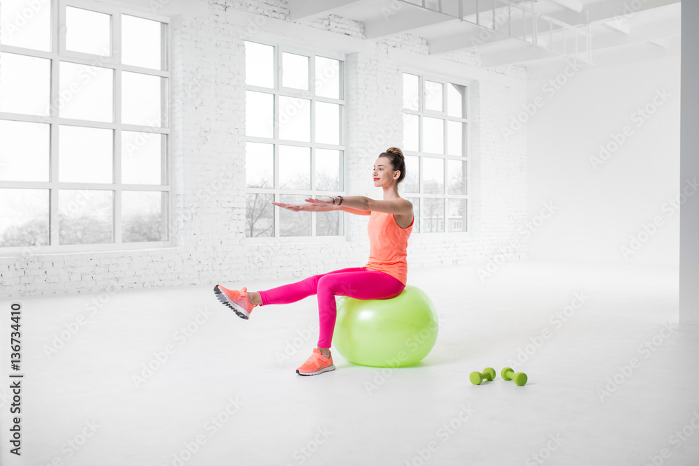 Young woman in colorful sportswear doing fitness with fitness ball in the white gym