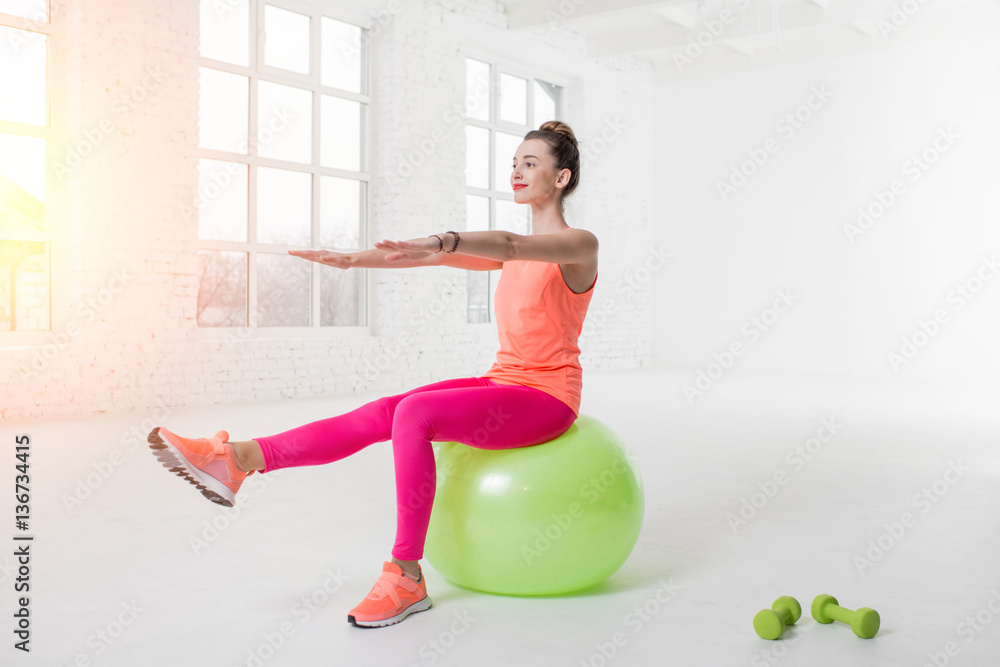 Young woman in colorful sportswear doing fitness with fitness ball in the white gym