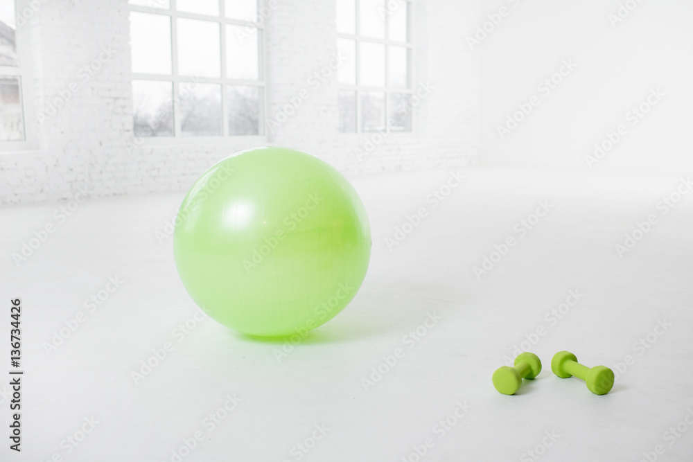 Fitness ball with dumbbells on the floor in the white room