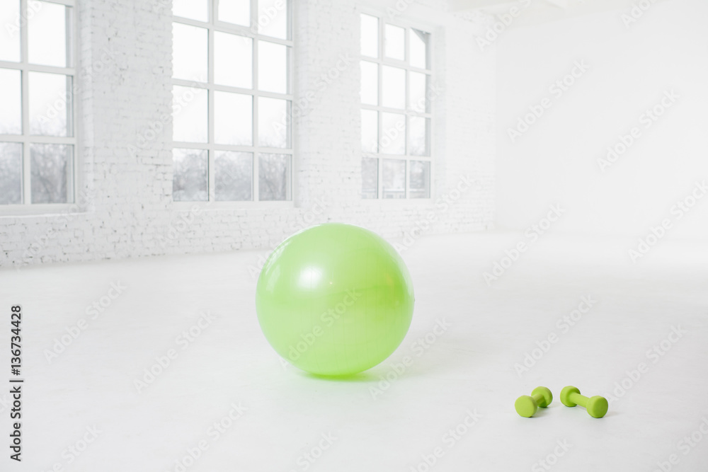 Fitness ball with dumbbells on the floor in the white room