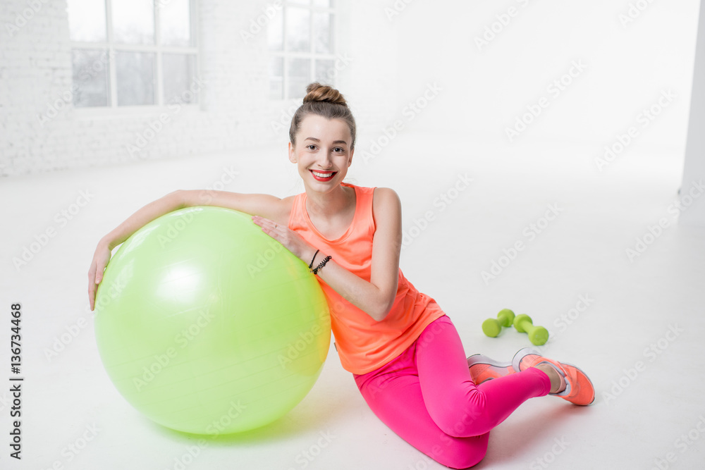 Portrait of a young woman in colorful sportswear lying with fitness ball on the floor in the white g