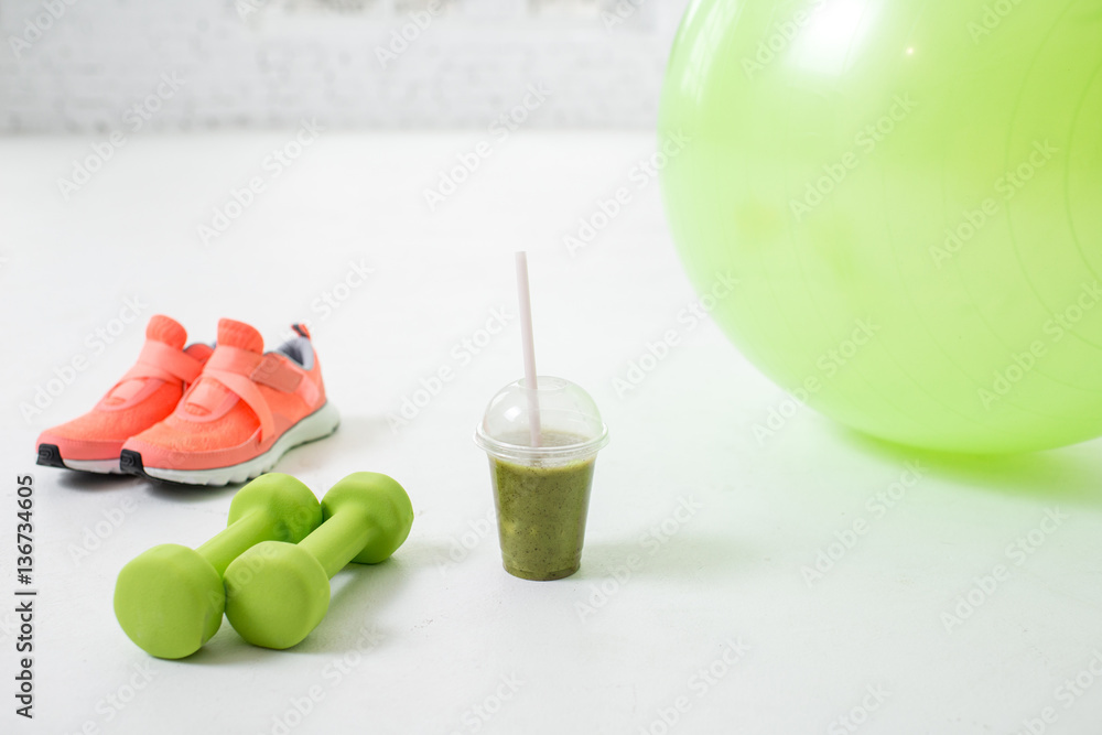 Fitness ball, dumbbells and glass with kiwi fresh on the floor in the white room