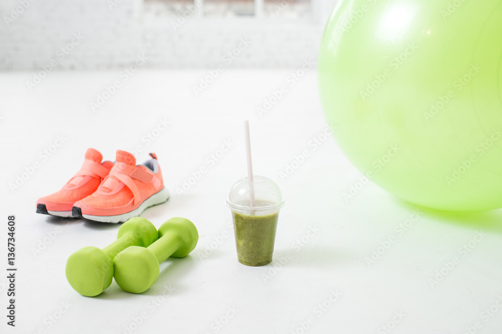 Fitness ball, dumbbells and glass with kiwi fresh on the floor in the white room