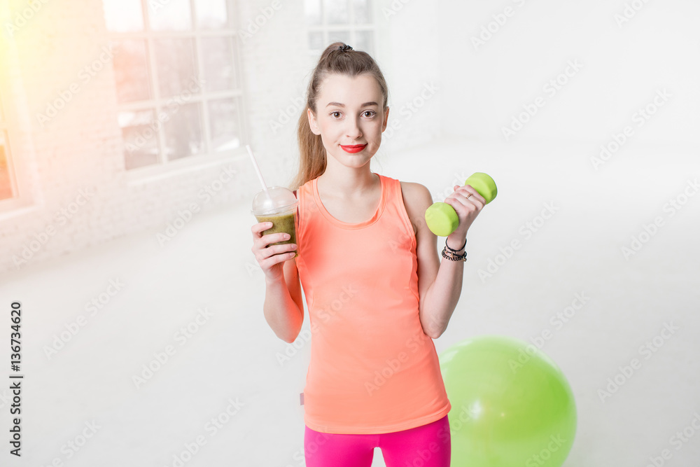 Portrait of young sport woman with kiwi fresh and dumbbells in the white gym