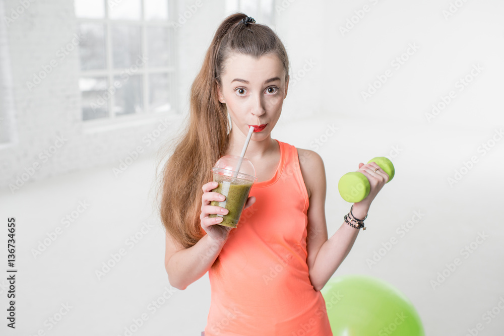 Portrait of young sport woman with kiwi fresh and dumbbells in the white gym