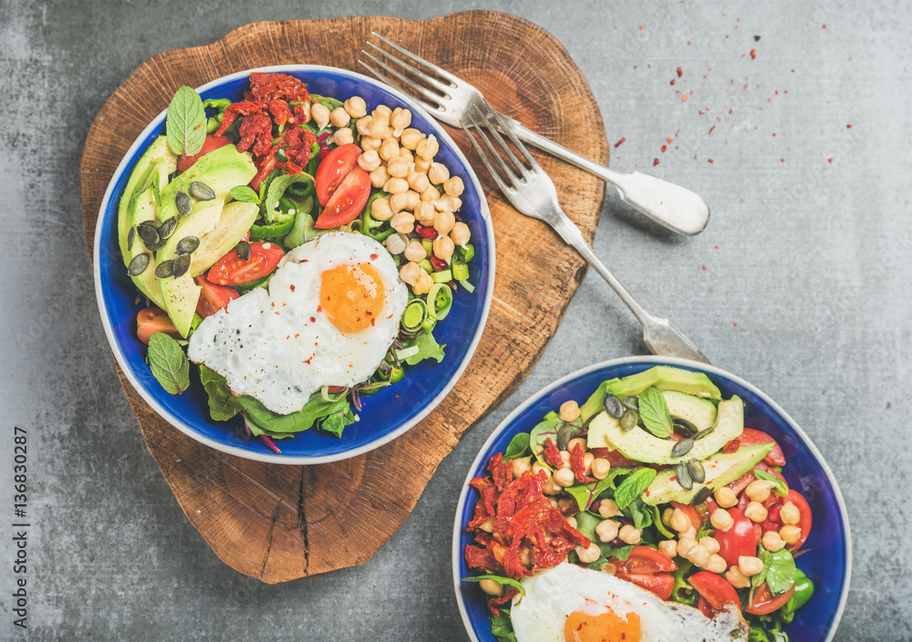 Healthy breakfast bowls with fried egg, chickpea sprouts, seeds, vegetables and greens over grey con