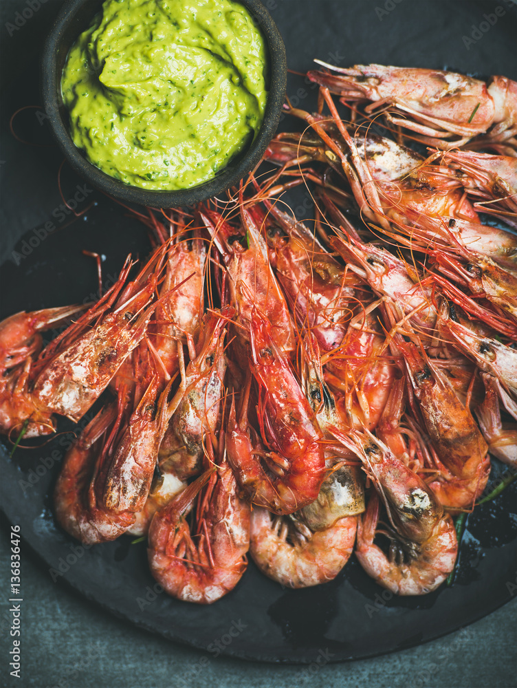 Roasted red shrimps with guacamole avocado sauce in slate stone black plate over grey concrete backg