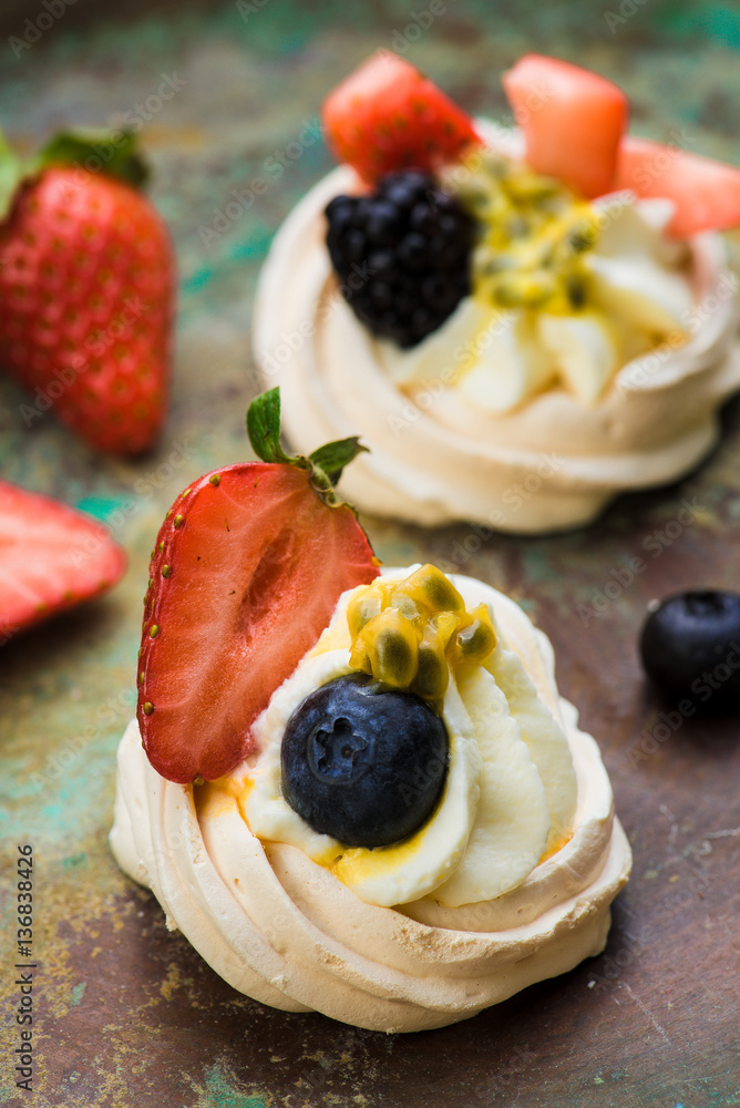 Mini Pavlova meringue cakes with berries and passion fruits on rustic vintage background. Top view.