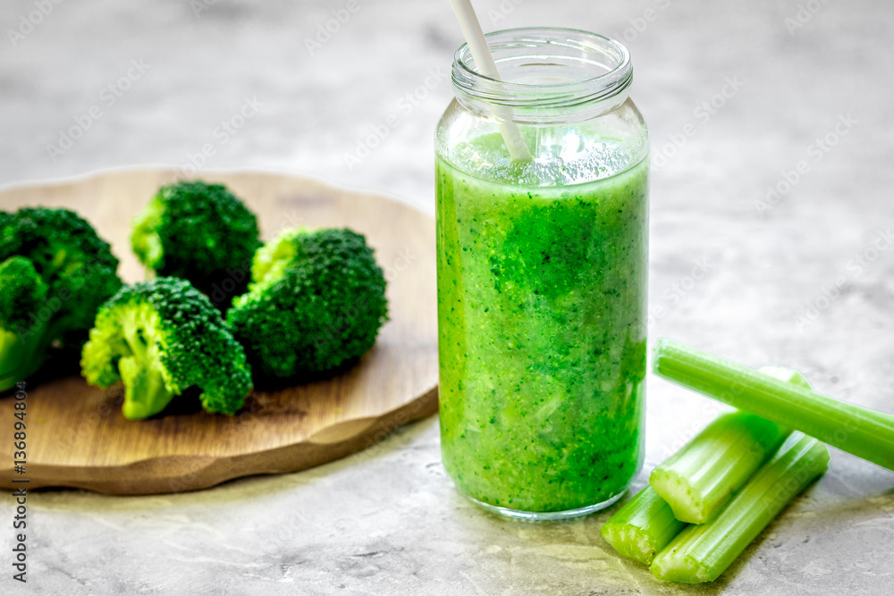 Green vegetable smoothie in glass at gray background