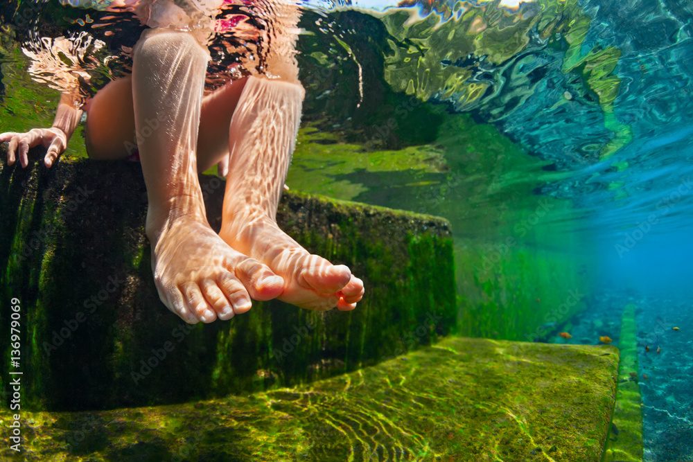 Happy person have fun at poolside edge. Funny under water photo of baby girl bare feet in natural po