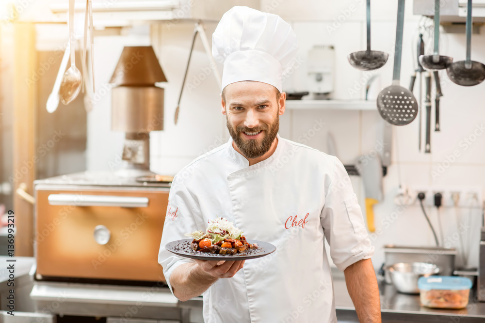 Portrait of chef cook in uniform standing with delicious dish at the kitchen