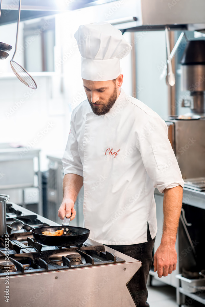 Handsome chef cook in uniform cooking food on the gas stove at the restaurant kitchen