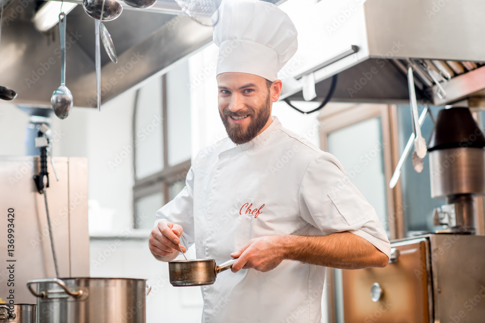 Handsome chef cook in uniform cooking food on the gas stove at the restaurant kitchen