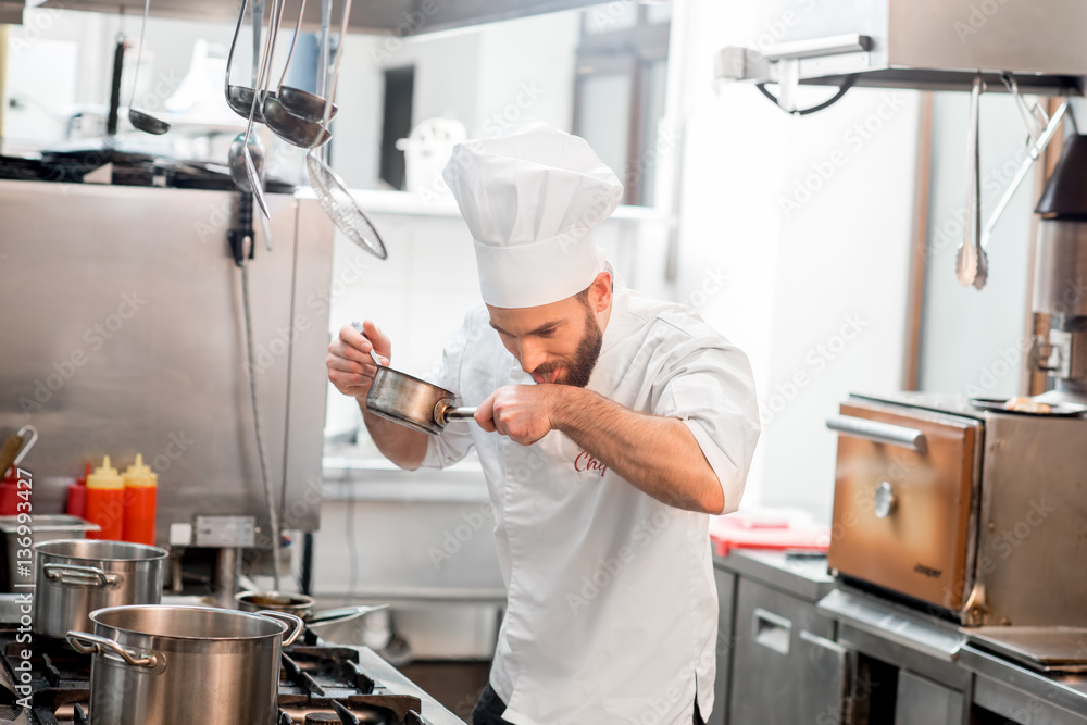 Chef cook in uniform cooking soup in the big cooker at the restaurant kitchen