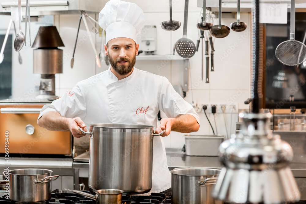 Chef cook in uniform cooking soup in the big cooker at the restaurant kitchen