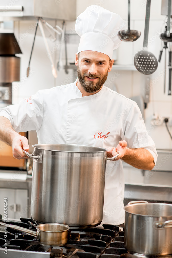 Chef cook in uniform cooking soup in the big cooker at the restaurant kitchen