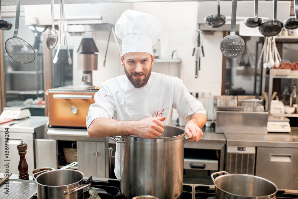 Portrait of a chef cook in uniform with big cooker at the restaurant kitchen