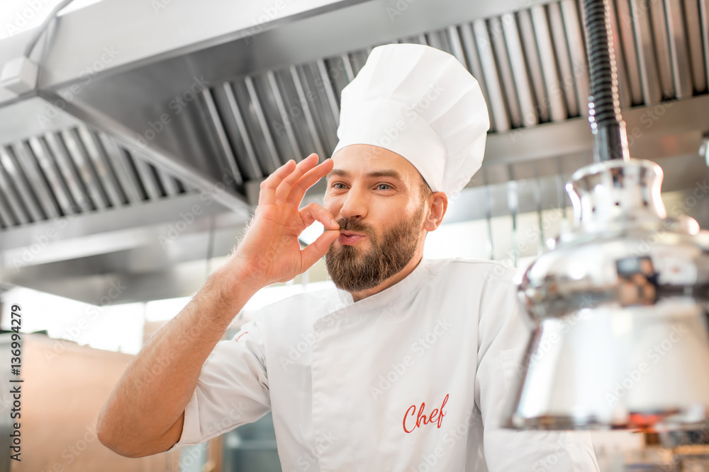 Portrait of a handsome chef cook in uniform showing delicious sign at the restaurant kitchen